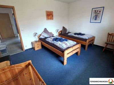 Das Bild zeigt das Schlafzimmer 2 in der Ferienwohnung 1 der Pension Quellenhof Altenau, ausgestattet mit 2 Einzelbetten, einem Kinderbett und Kinderhochstuhl.