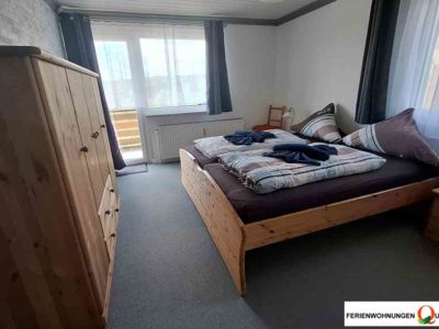 Schlafzimmer 1 mit Doppelbett, Nachttischcen, Kleiderschrank und Zugang zum Balkon in Ferienwohnung 1 der Pension Quellenhof in Altenau