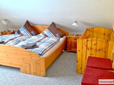 Das Schlafzimmer 1 der Ferienwohnung Nr. 5 bietet ein Doppelbett, Konsolen, Kleiderschrank und en Kinderbett