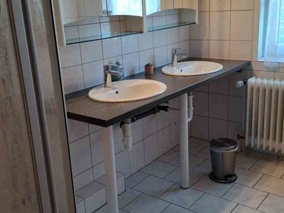 Blick in das große Badezimmer mit Dusche, 2 Waschbecken, 2 Spiegelschränken, WC und Waschmaschine. Diese Ferienwohnung wird vom Quellenhof Altenau im Harz, Kreis Goslar, angeboten.