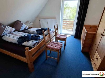 Blick ins Schlafzimmer 1 der Ferienwohnung 2, pension Quellenhof Altenau. Ausgestattet mit Doppelbett, Nachttischen, Babybett, Kleiderschrank und 2 Stühlen zur Kleiderablage. Mit Balkonzugang.