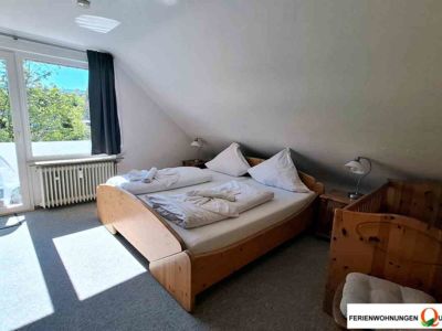Das Schlafzmmer 1 in Ferienwohnung 5 der Pension Quellenhof in Altenau/Oberharz bietet ein Doppelbett, ein Kinderbett, Kleiderschrank und besitzt einen Balkonzugang.