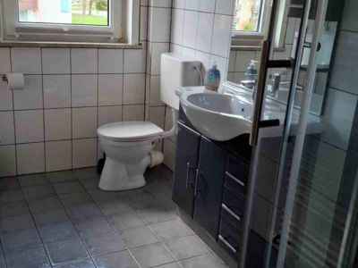 Schön ausgestattetes Badezimmer der Ferienwohnung 7 der Pension Quellenhof Altenau mit Dusche, WC und Waschtisch mit Spiegel und Unterschrank.
